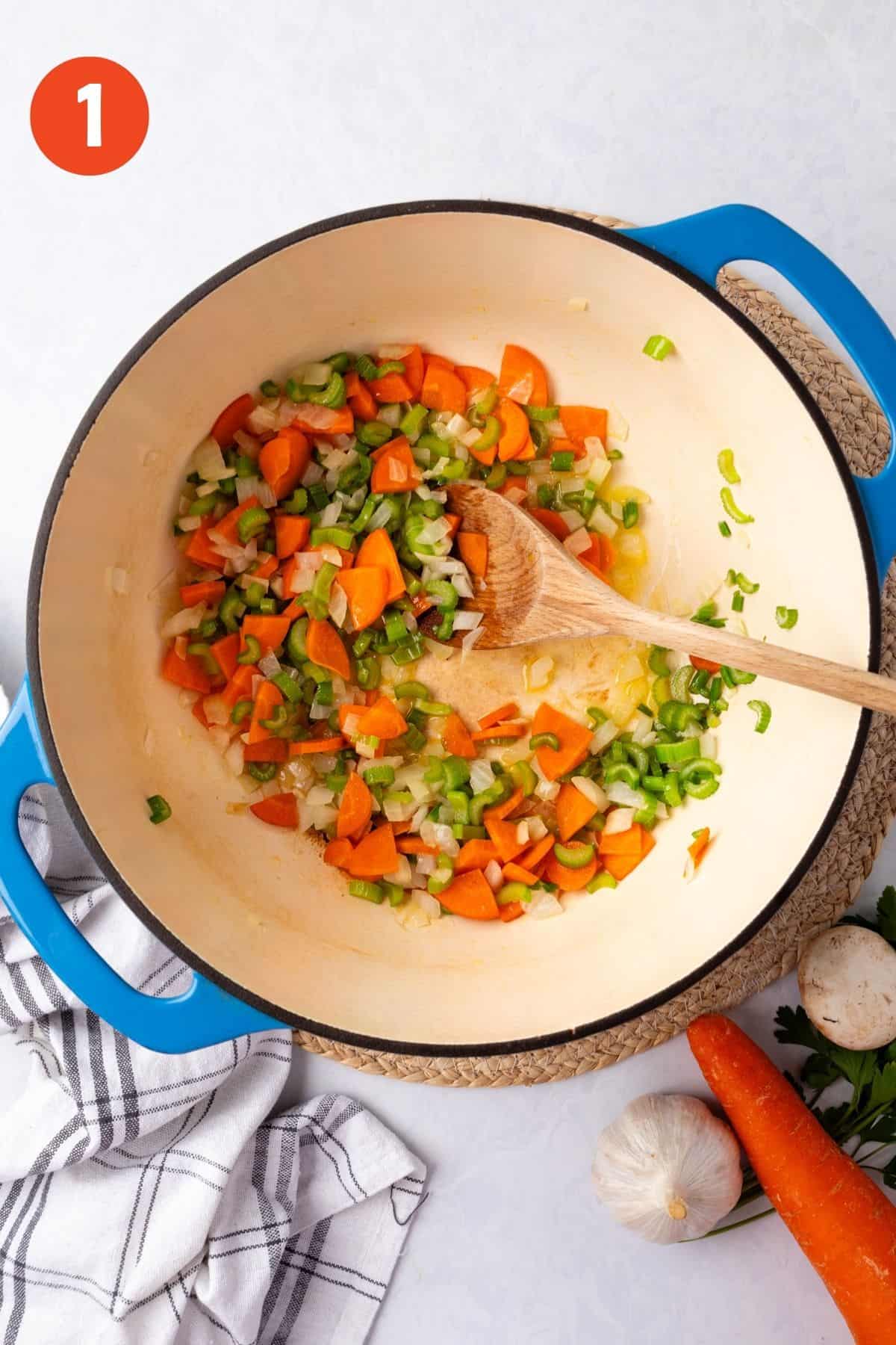 Celery, onions, and carrots cooking in a blue Dutch oven.