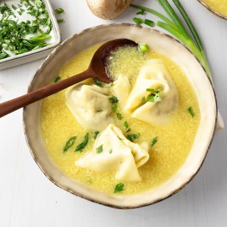 A bowl of wonton egg drop soup with a spoon resting in the bowl.