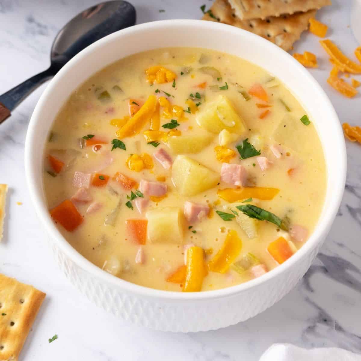 A white bowl with ham and potato soup.