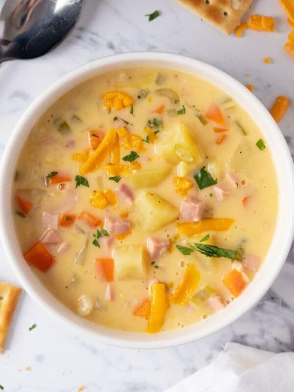 A bowl of cheesy ham and potato soup with crackers on the table next to the bowl.