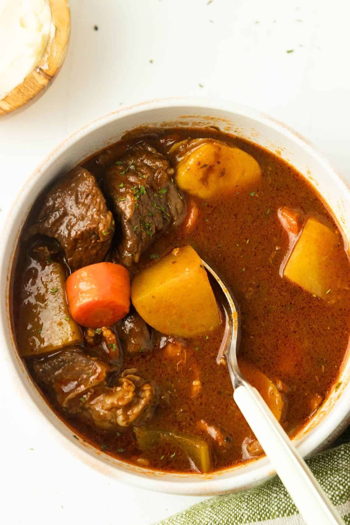 A bowl of Irish stew with a spoon scooping out a potato.