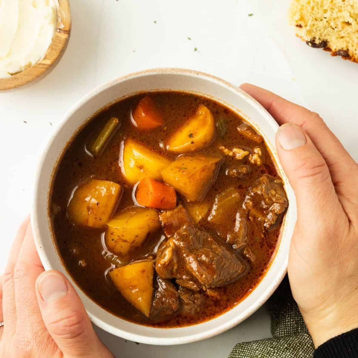 Hands picking up a bowl of Irish stew.
