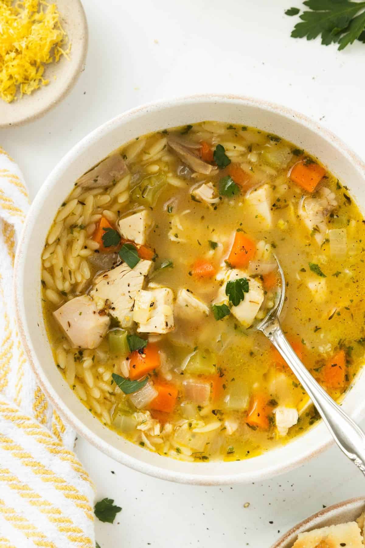 Lemon chicken orzo soup in a bowl being scooped up with a spoon.
