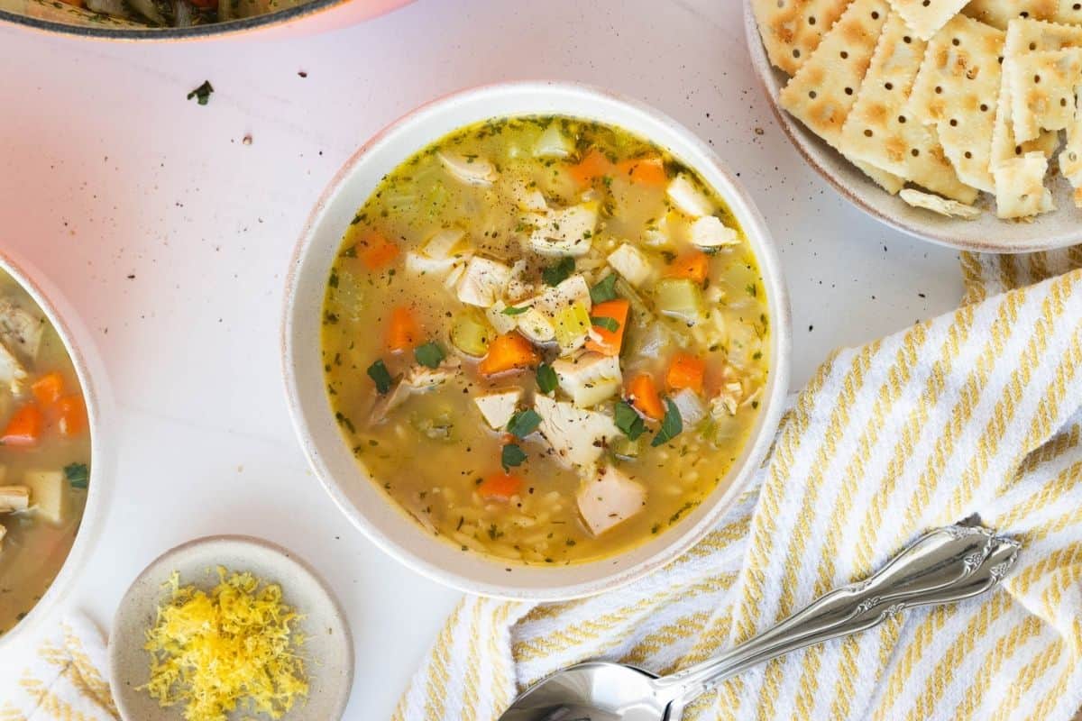 Lemon chicken orzo soup in a bowl on a table with crackers on the side.