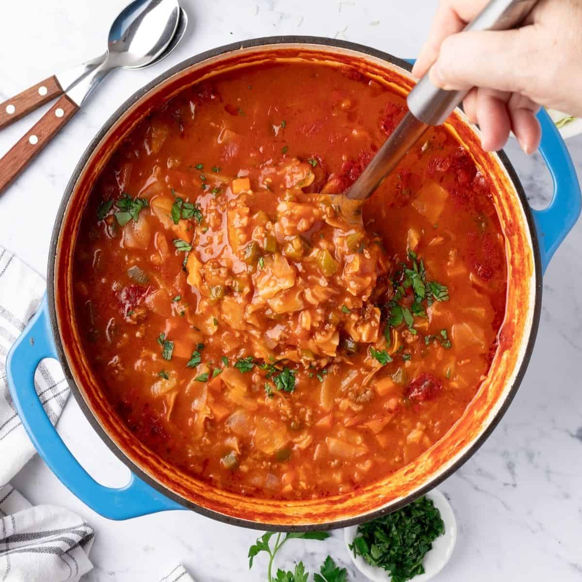 Cabbage roll soup in a large Dutch oven with a ladle full held over the pot.