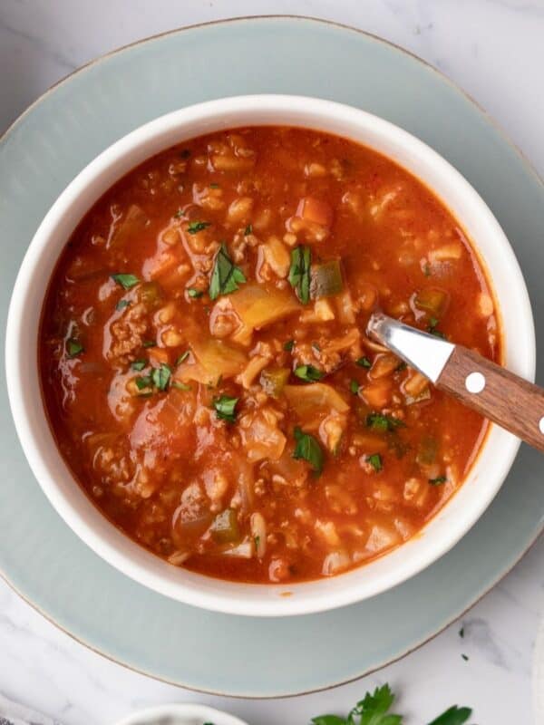 A bowl of unstuffed cabbage soup on a plate with a spoon resting in the bowl.