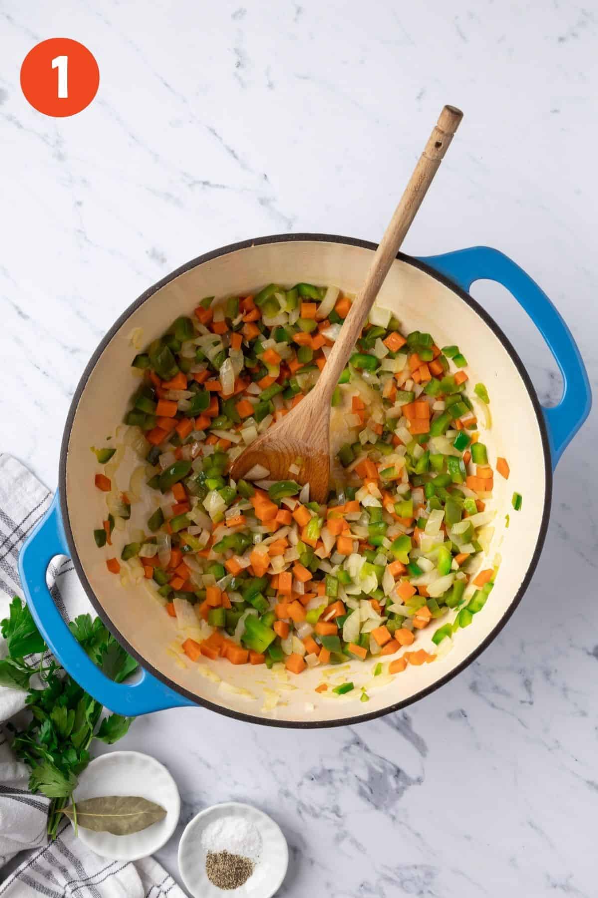 Cooking the onion, carrots, and bell pepper in a Dutch oven.