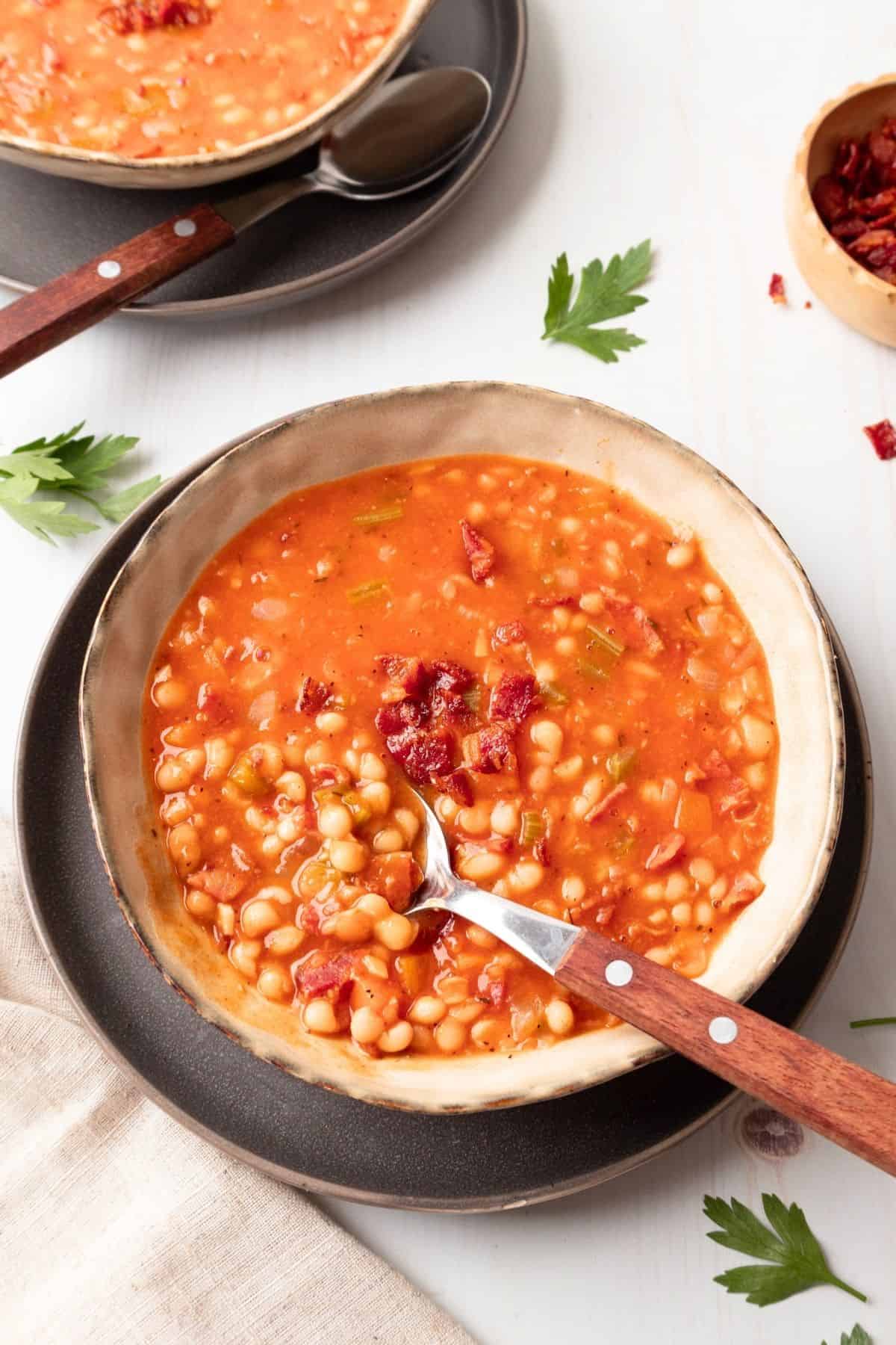 A spoon taking out some bean and bacon soup out of the bowl.
