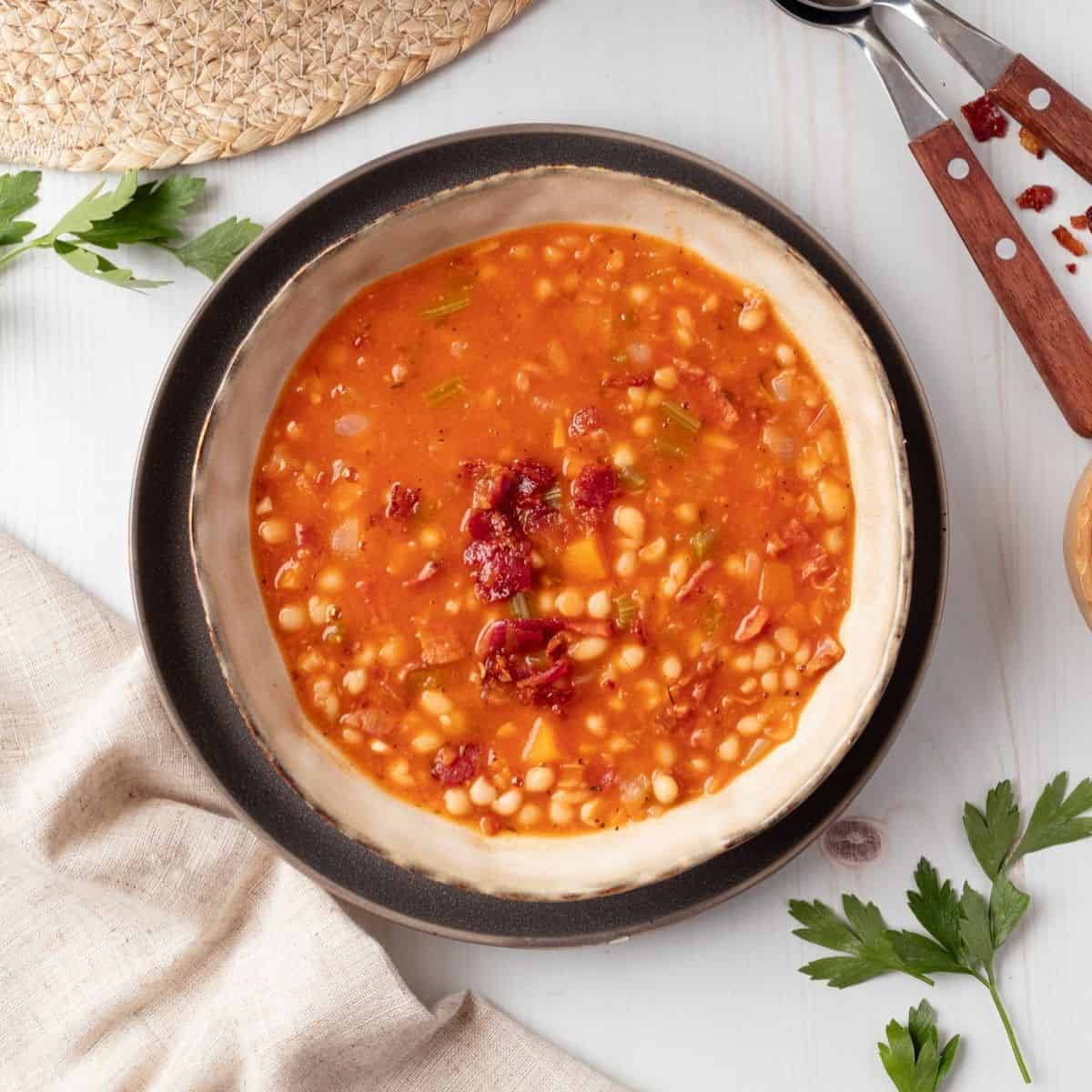 A white bowl of bean and bacon soup.
