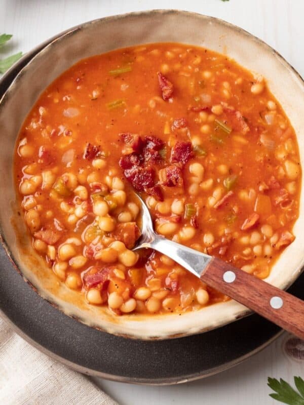 A bowl of bean and bacon soup and a spoon taking some out.