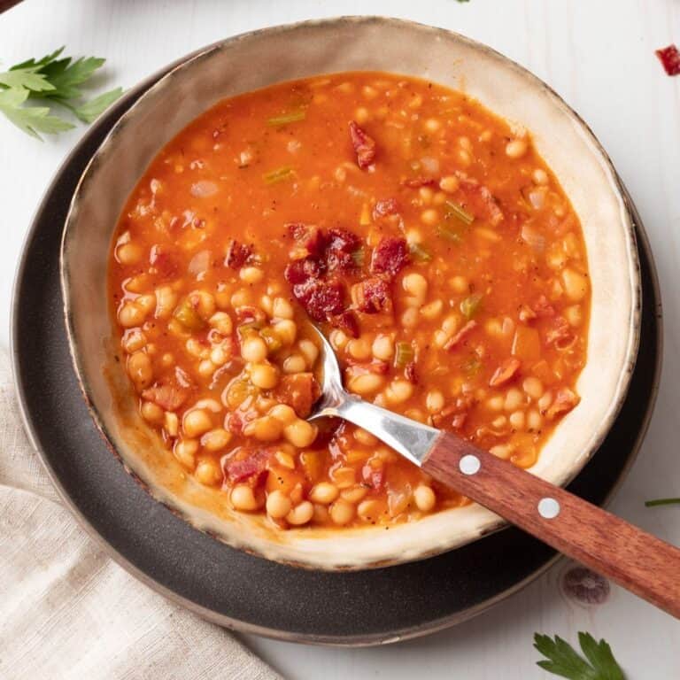 A bowl of bean and bacon soup and a spoon taking some out.