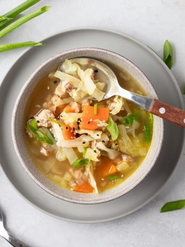 Egg roll soup in a bowl on a gray plate with a spoon scooping some out.