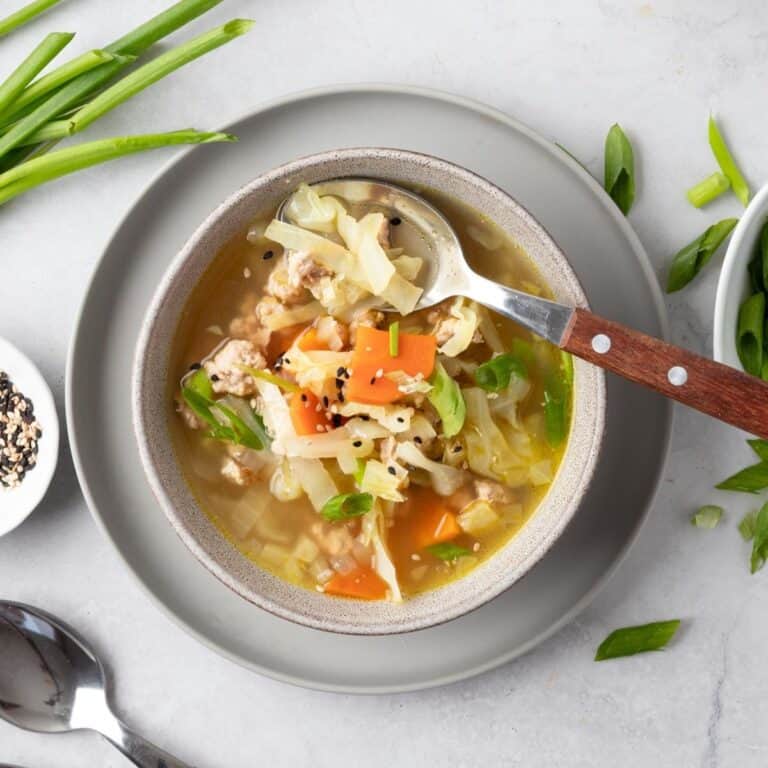 Egg roll soup in a bowl on a gray plate with a spoon scooping some out.