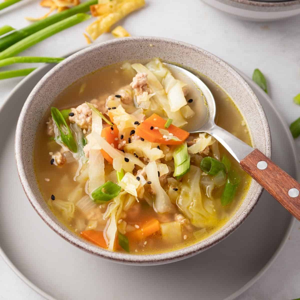 A bowl filled with egg roll soup and a spoon resting on the side.