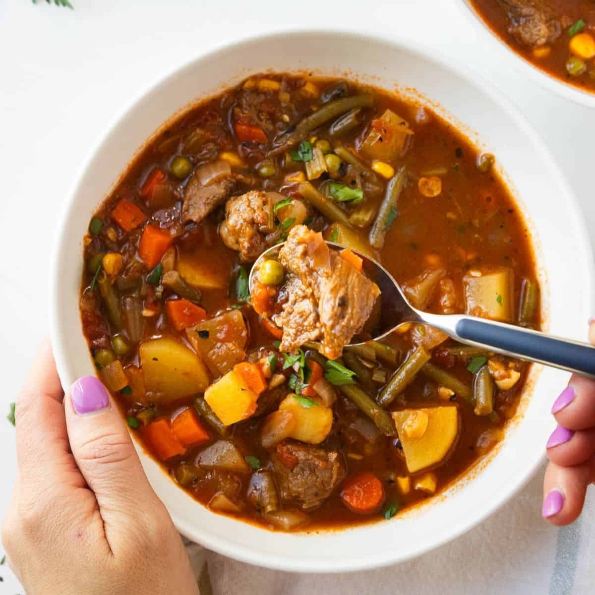 Vegetable beef stew being scooped up with a spoon.