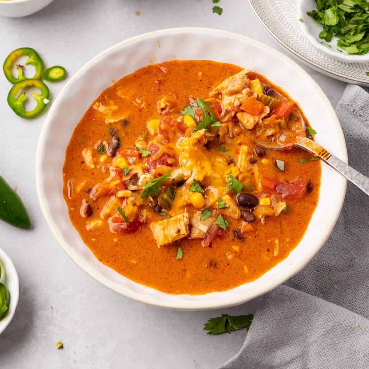 A spoon taking some cheesy chicken enchilada soup out of a bowl.