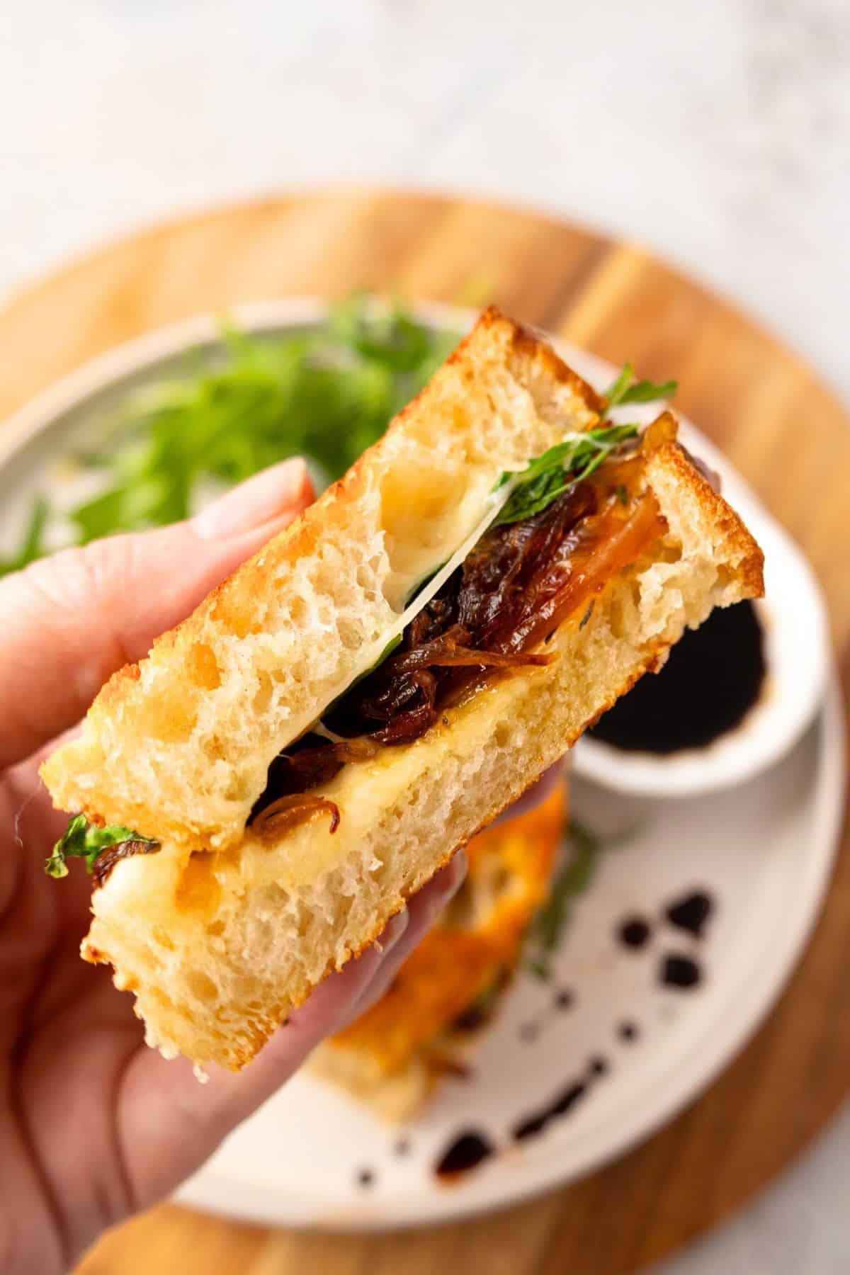 A hand holding up a French onion grilled cheese up over the plate.