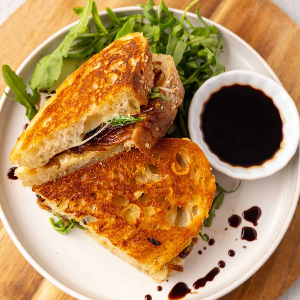 French onion grilled cheese sliced in half and on a white plate.