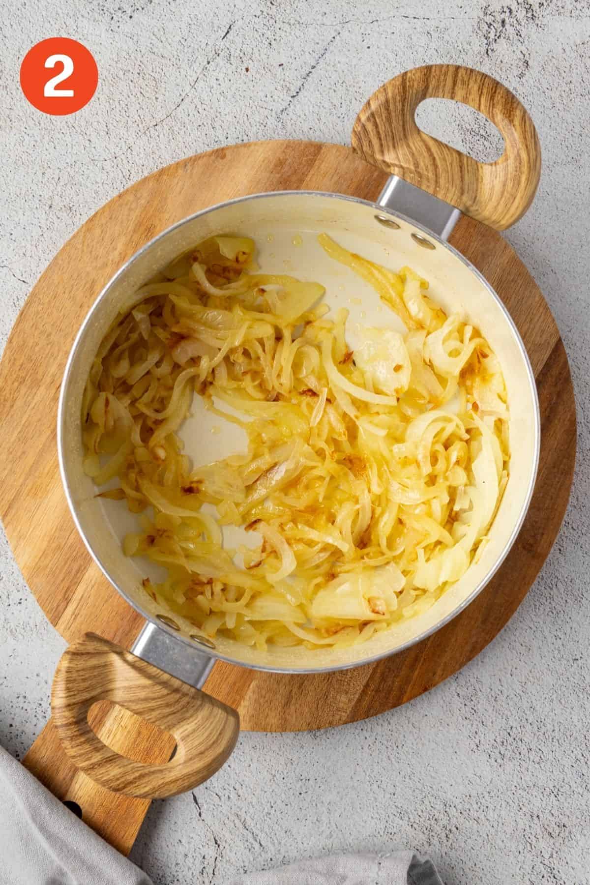 Onions cooking in a pan starting to soften and brown.