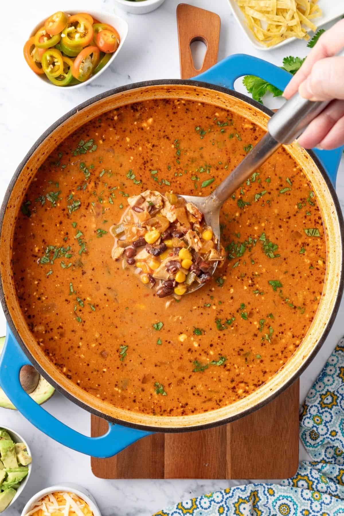 Creamy chicken taco soup in a Dutch oven with a ladle lifting up a serving.