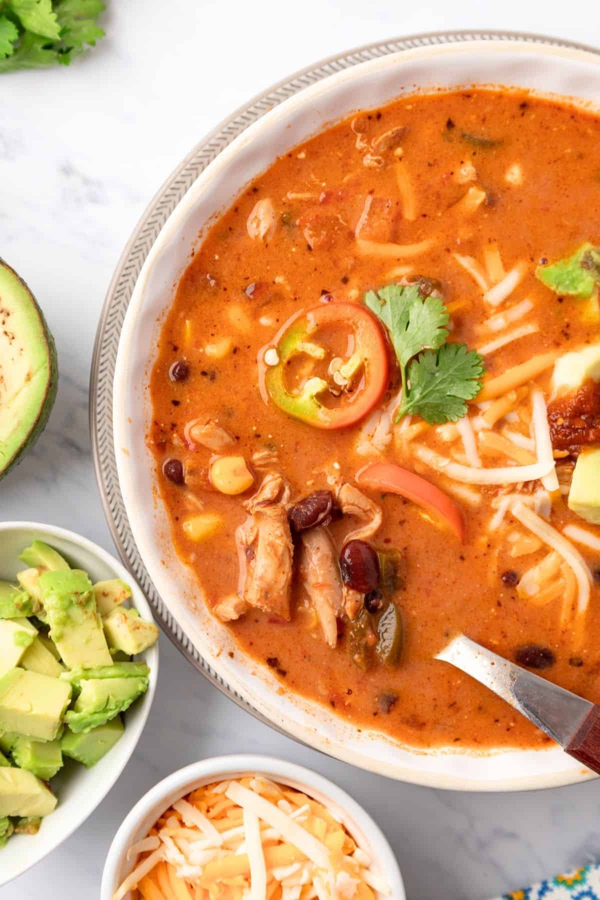 A bowl of chicken taco soup with cream cheese and a spoon lifting up a bite with chicken adn beans.