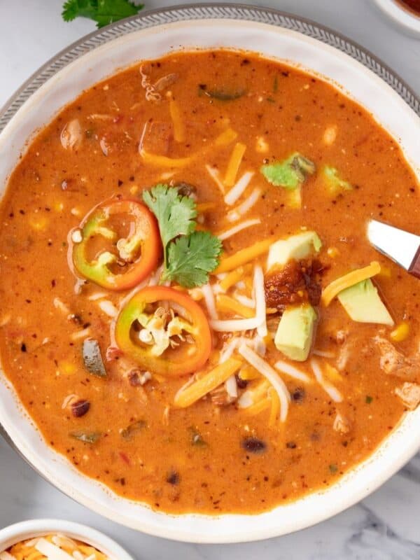 A white bowl of chicken taco soup with a spoon resting to the side.