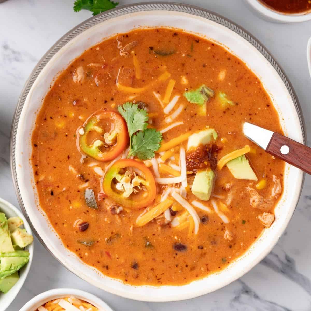 A white bowl of chicken taco soup with a spoon resting to the side.