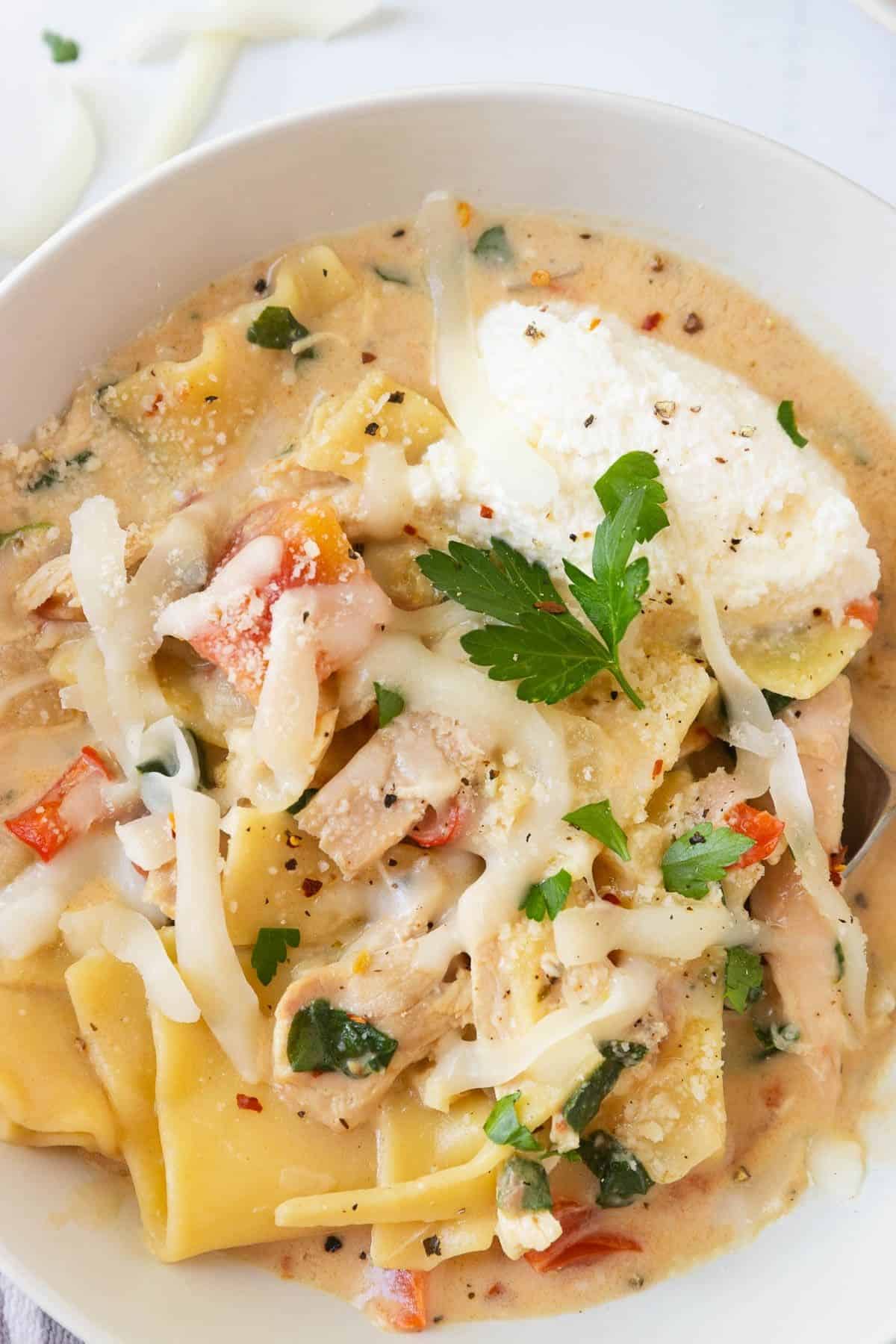 A bowl of white chicken lasagna soup garnished with ricotta.