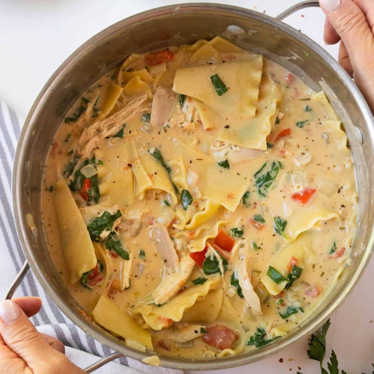 A pot of white chicken lasagna soup with hands on the handles.