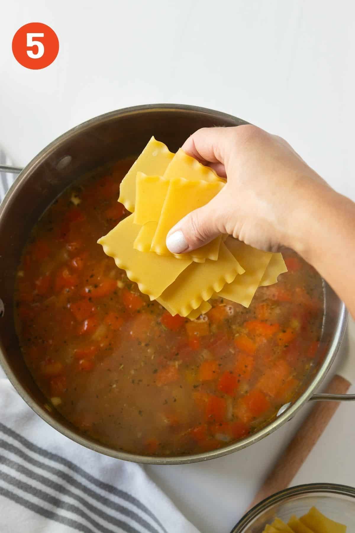 Adding lasagna noodles to the pot of soup.