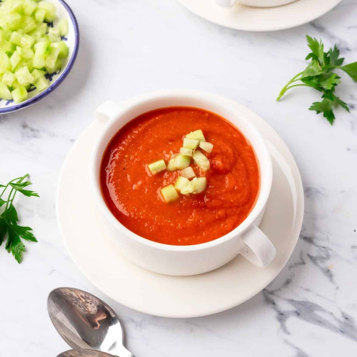 A bowl of cold tomato soup garnished with diced cucumber.