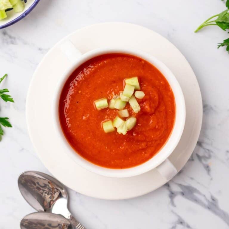 A bowl of cold tomato soup made with roasted tomatoes and garnished with cucumber.