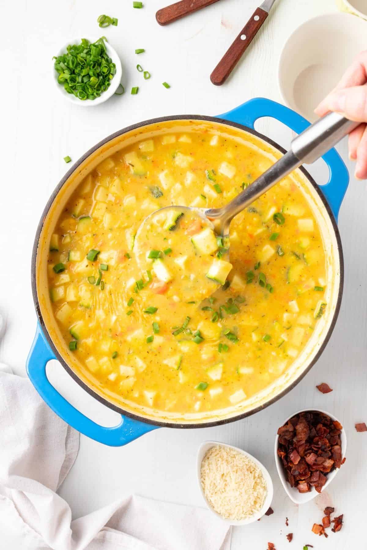 A pot of zucchini and corn chowder with a ladle dipping into the pot.