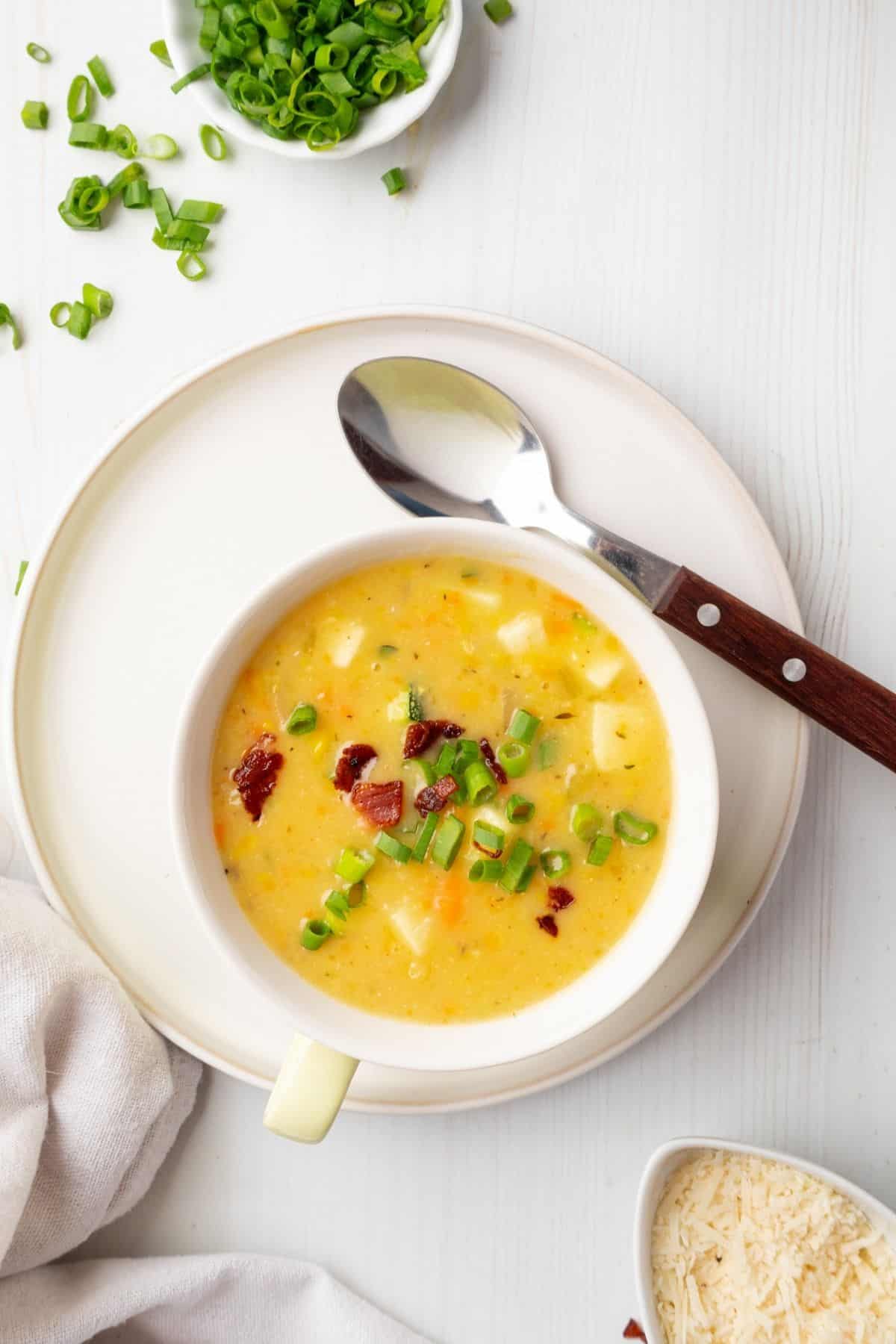 Bowl of corn and zucchini soup with a spoon resting on a plate.
