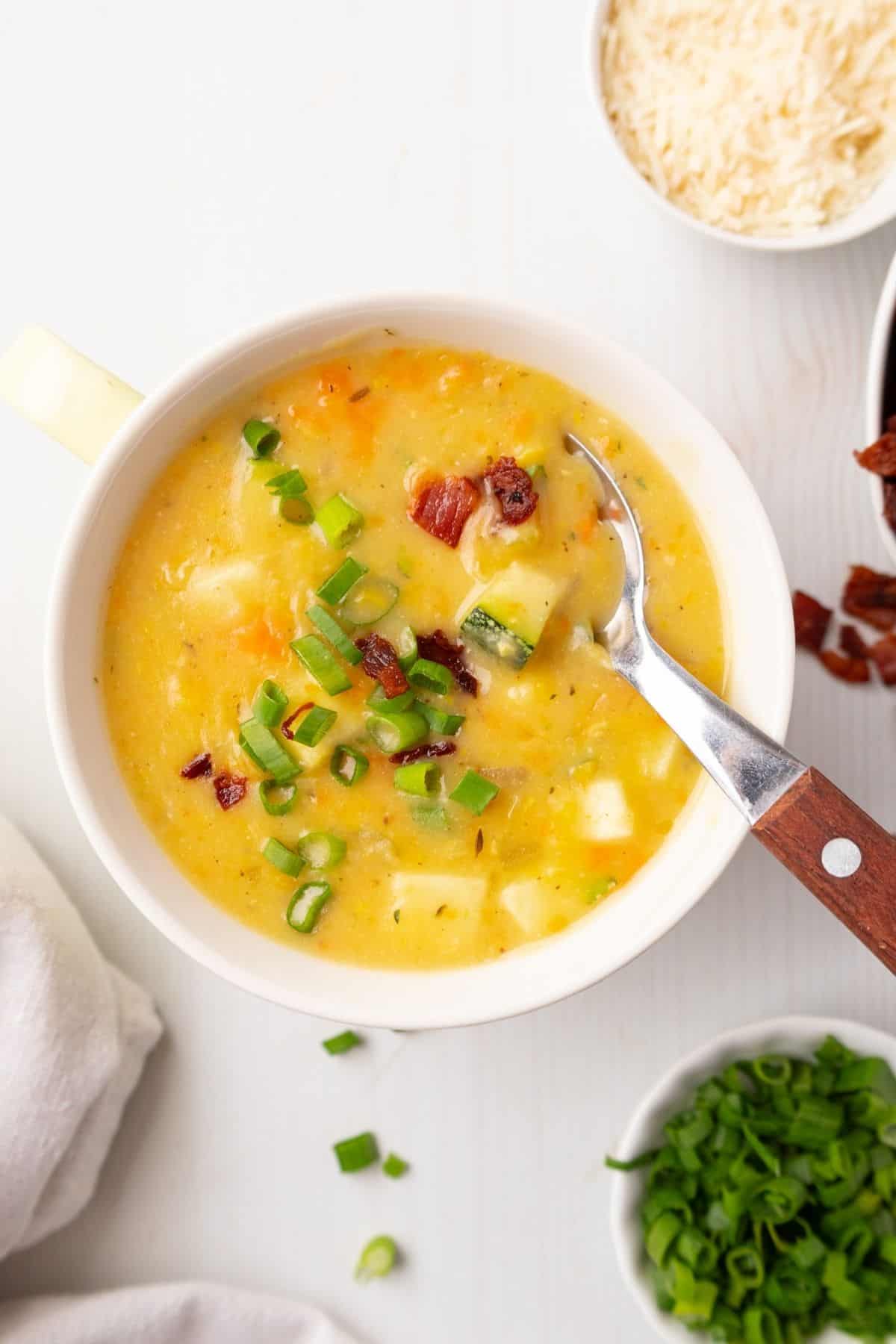 A bowl of zucchini corn chowder with a spoon resting in the bowl.