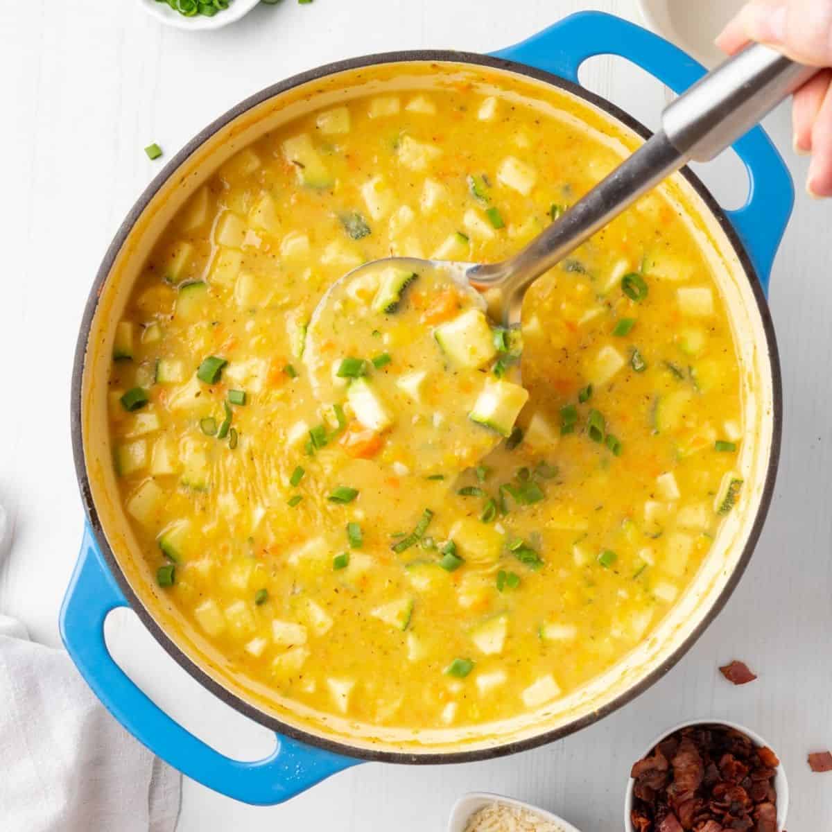 A ladle lifting up a scoop of zucchini corn chowder.