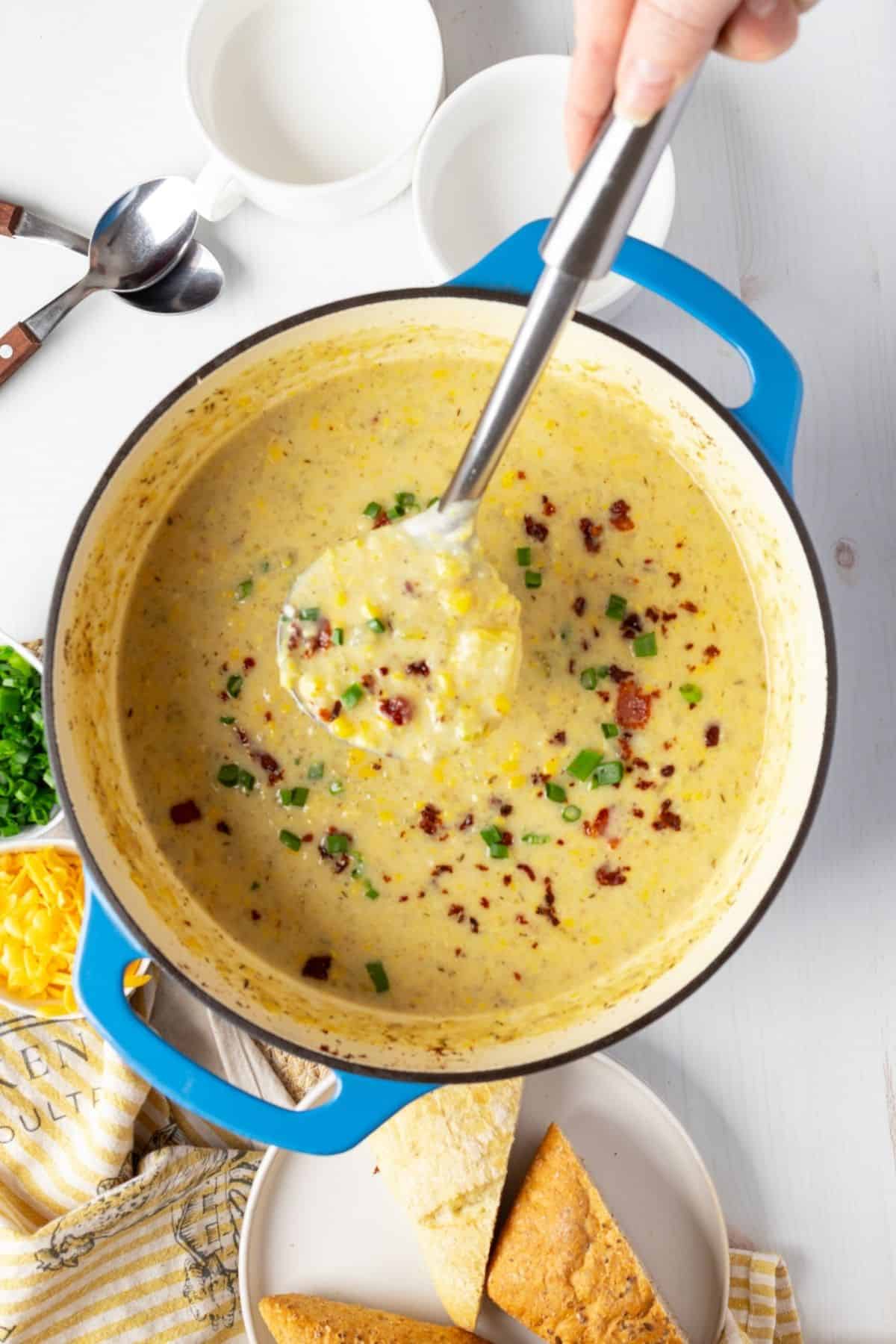 Creamy potato corn chowder in a blue pot with bacon bits and herbs on top.