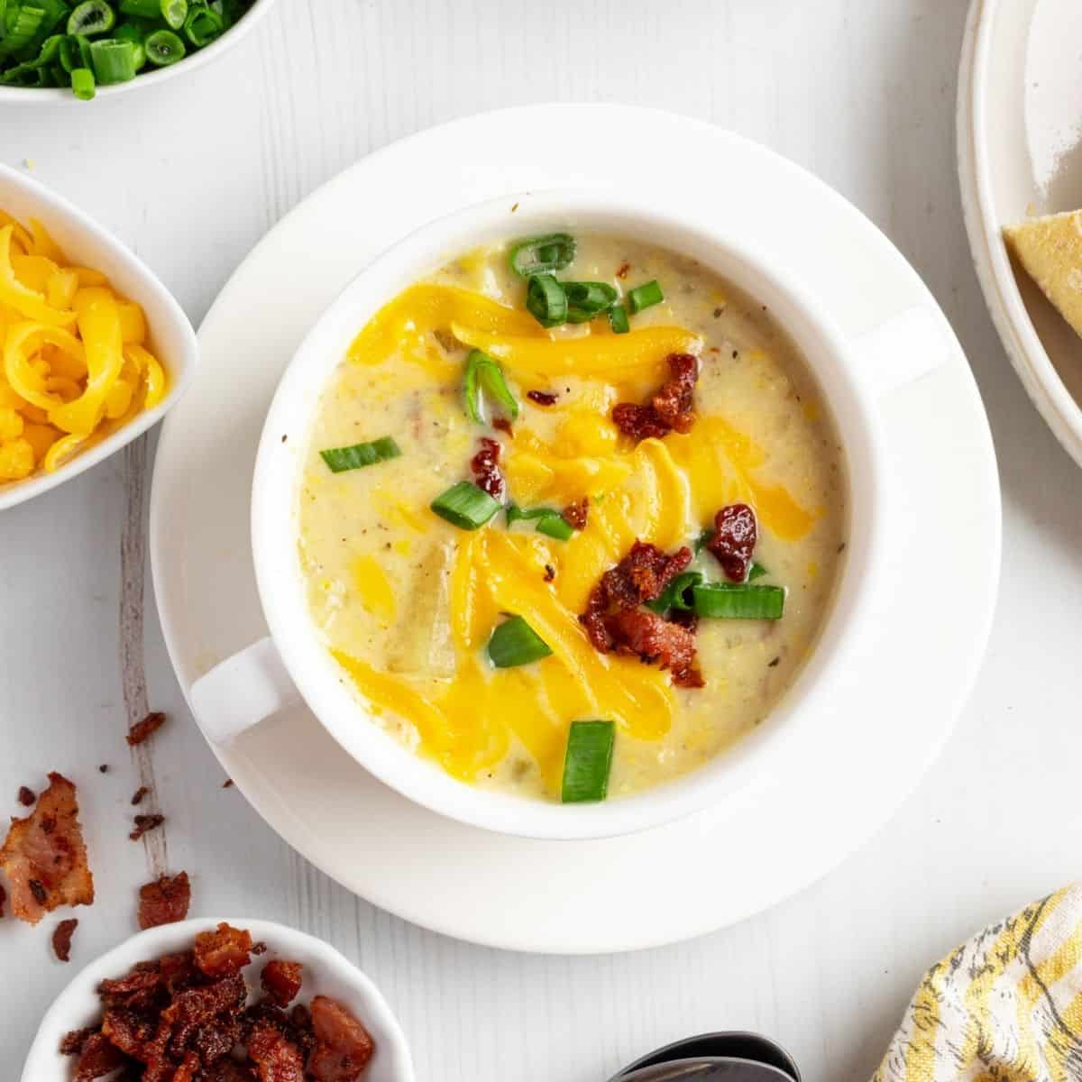 Creamy potato corn chowder garnished with green onions and bacon bits in a white bowl.