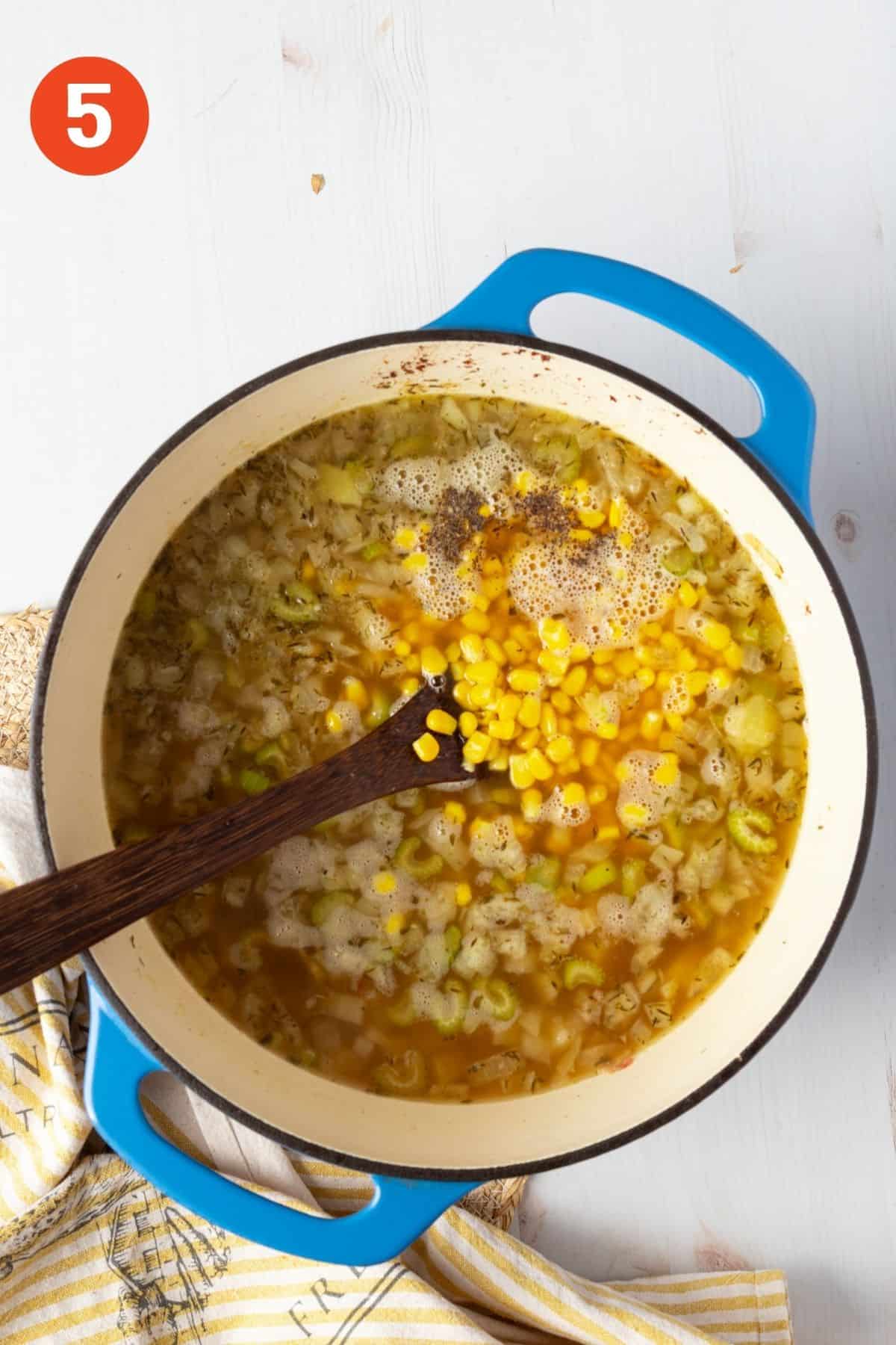 Potato corn chowder cooking with corn added to the pot with a wooden spoon.