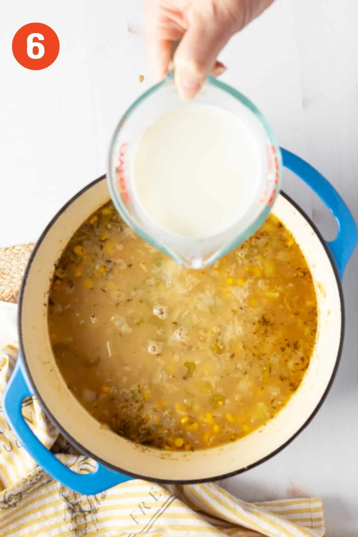 Pouring milk into potato corn chowder in a blue pot.