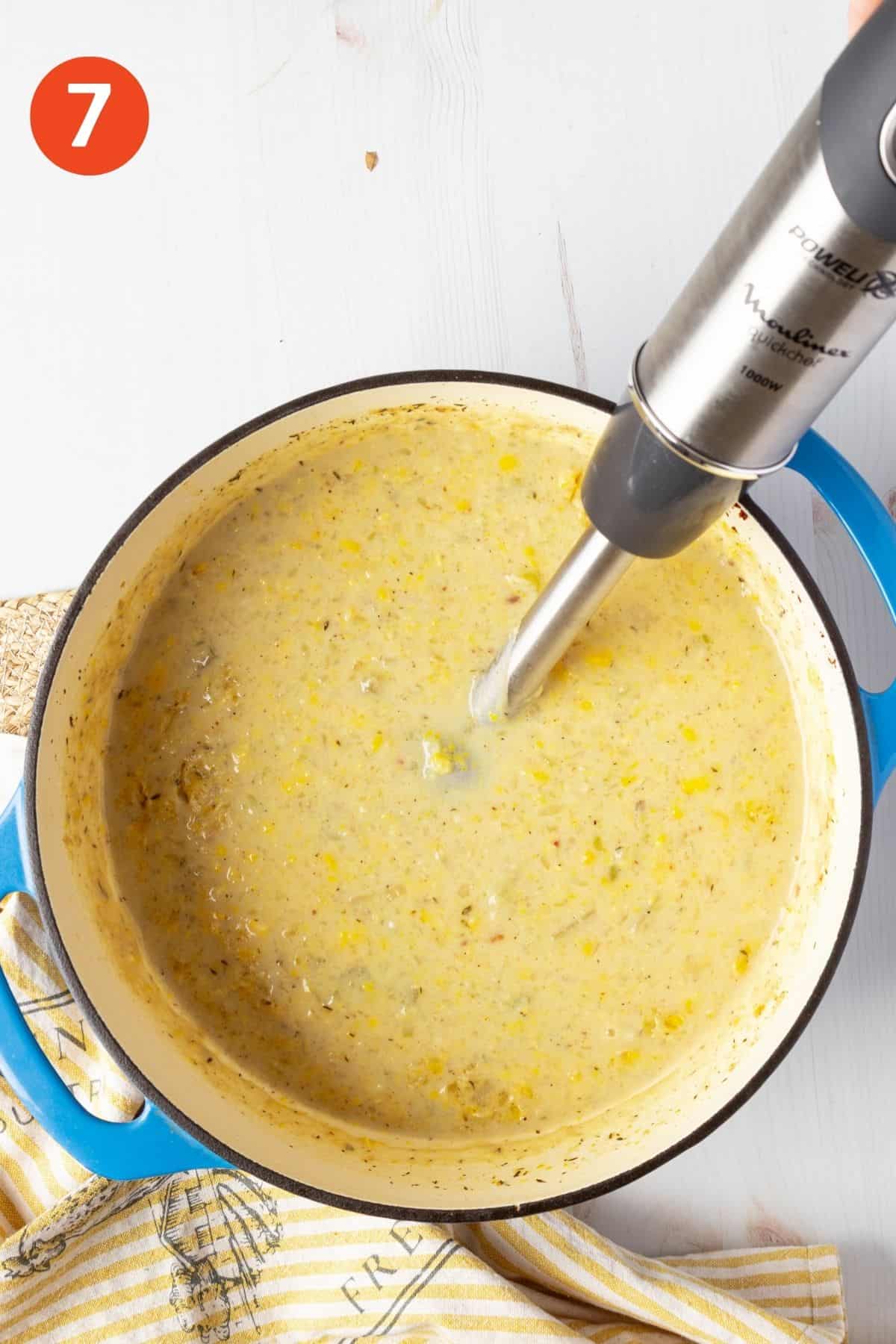 Blender blending creamy potato corn chowder in a blue pot.
