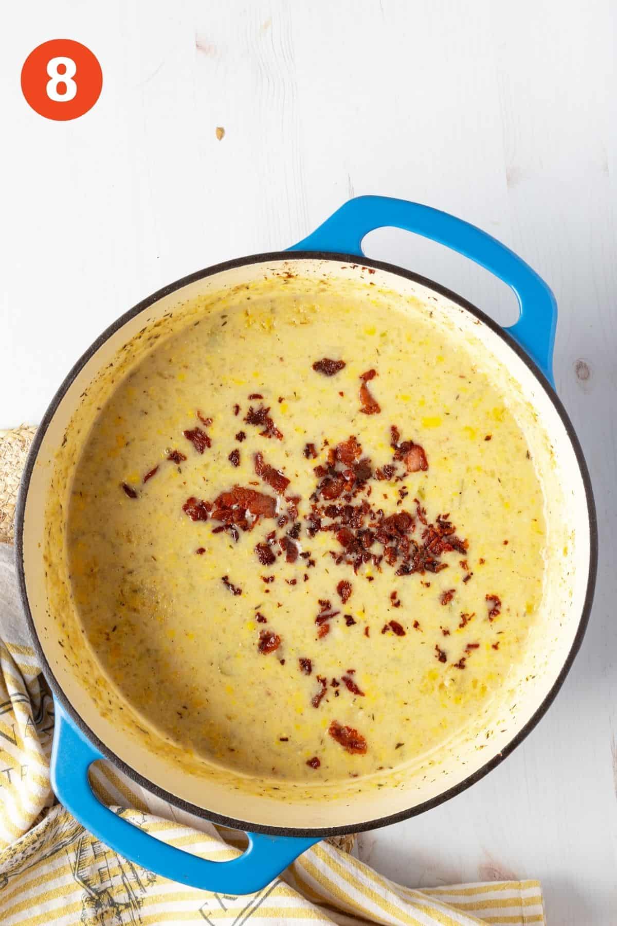 Creamy potato corn chowder topped with bacon bits in a blue pot.