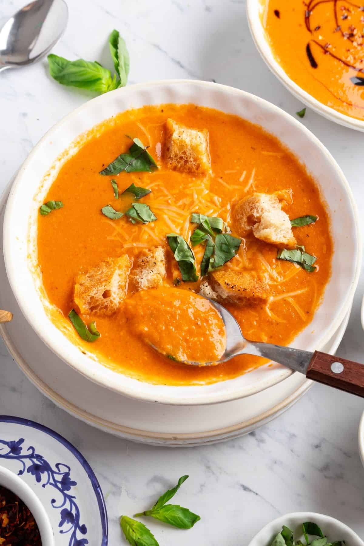 A bowl of roasted tomato soup with basil topped with croutons and fresh basil.