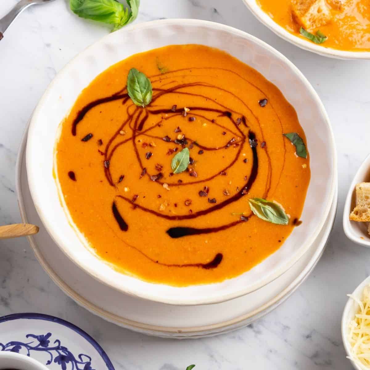 Roasted tomato basil soup with balsamic syrup drizzled and fresh basil on top.