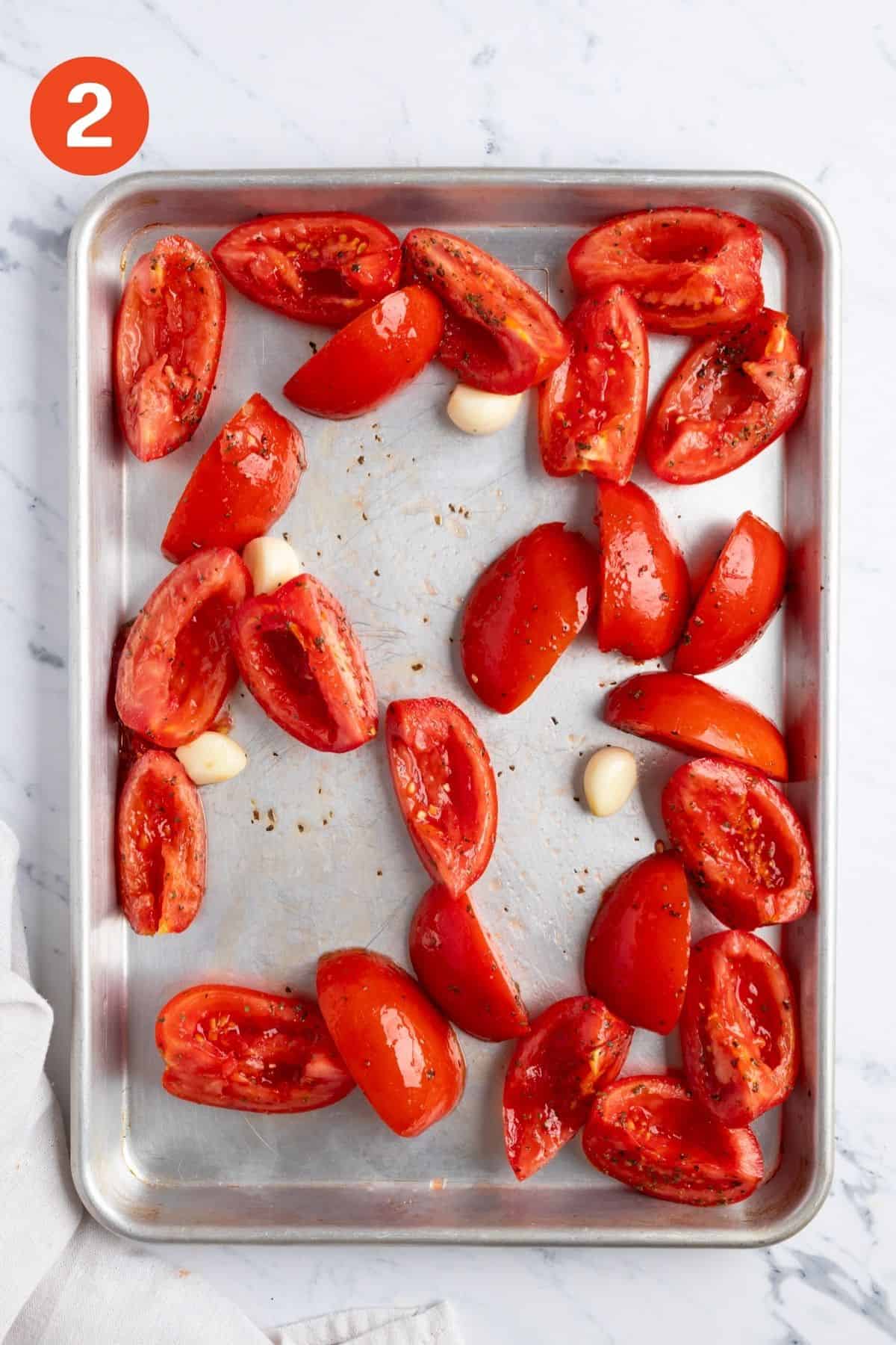 Tomatoes and garlic spread out on a baking pan.