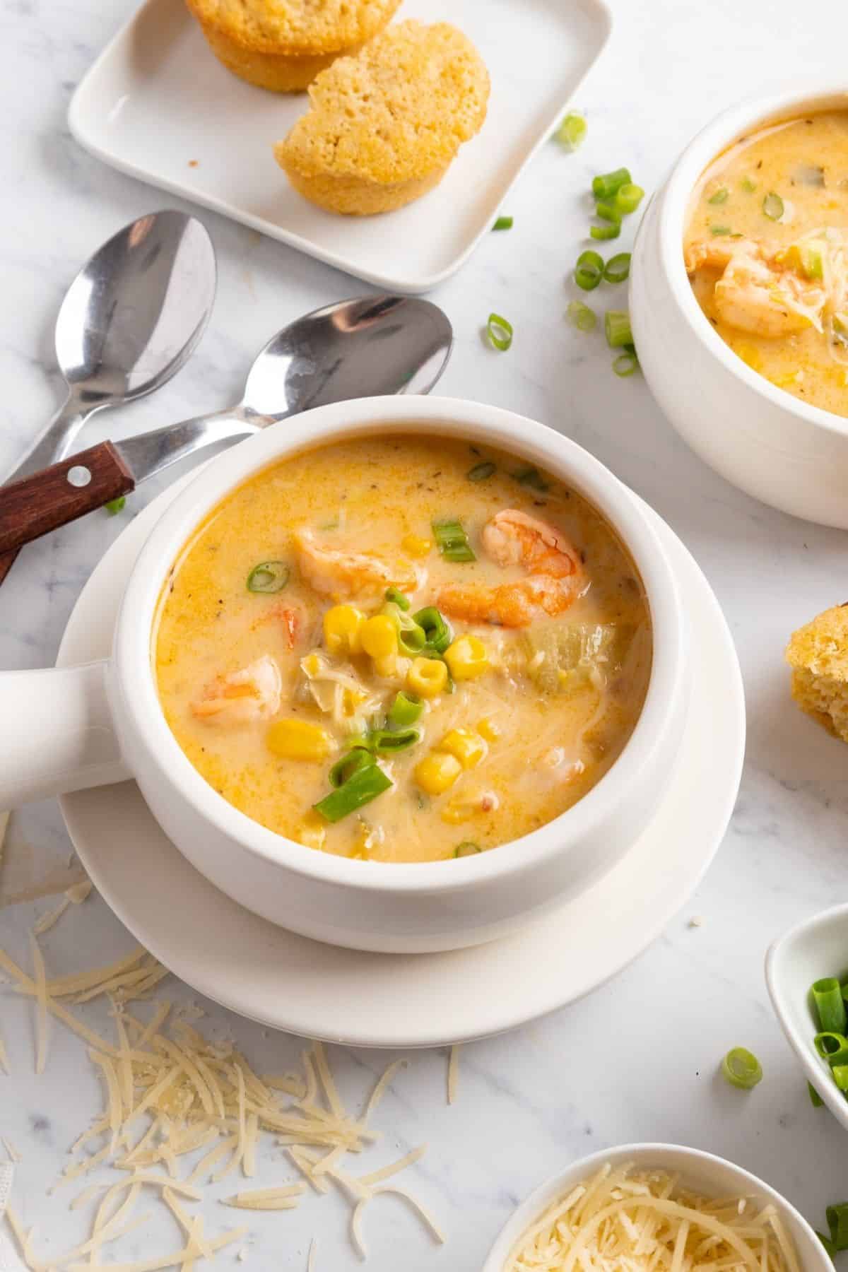 A bowl of corn shrimp chowder on a white plate with another bowl to the side.