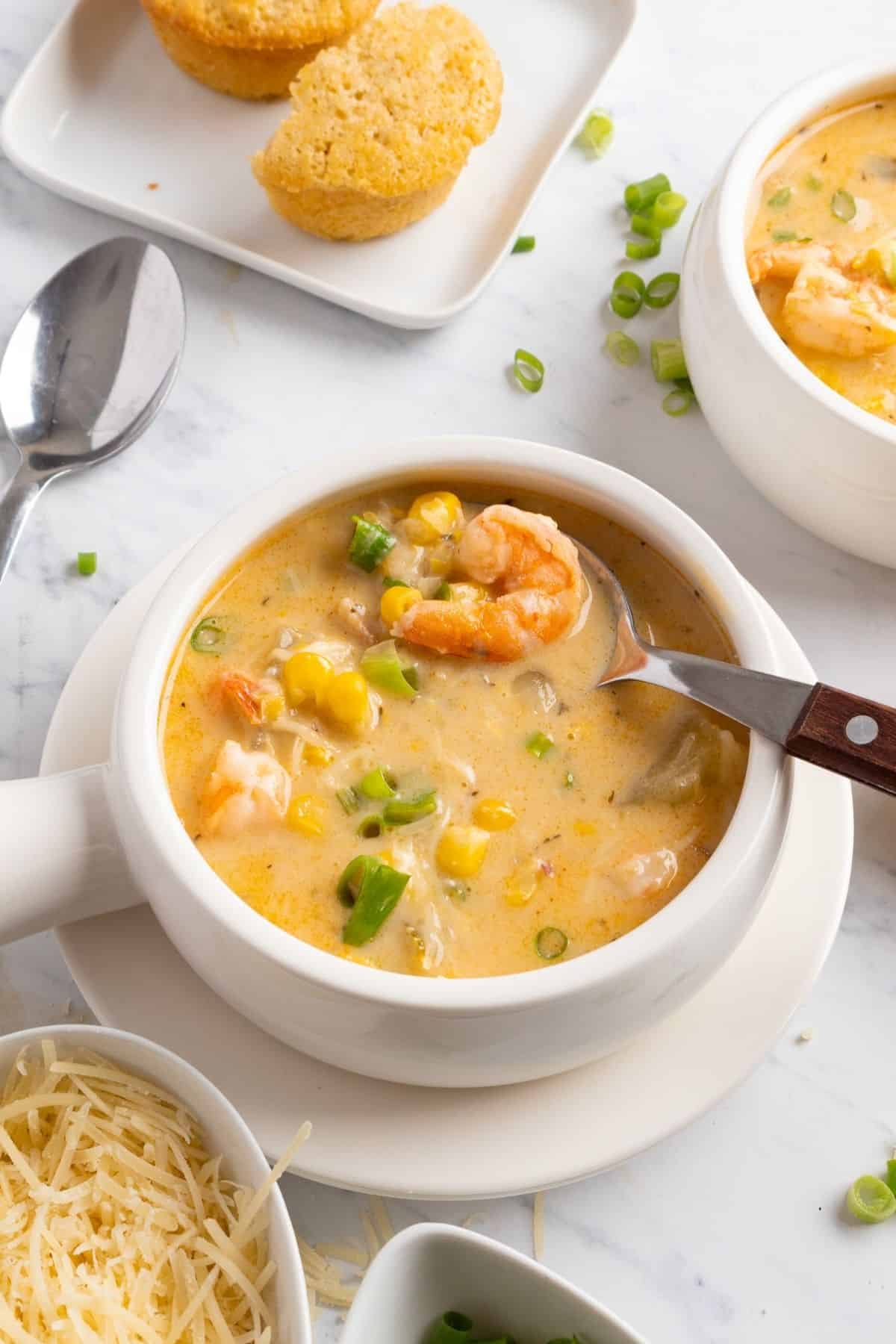 A bowl of shrimp corn chowder with a spoon lifting up a bite.