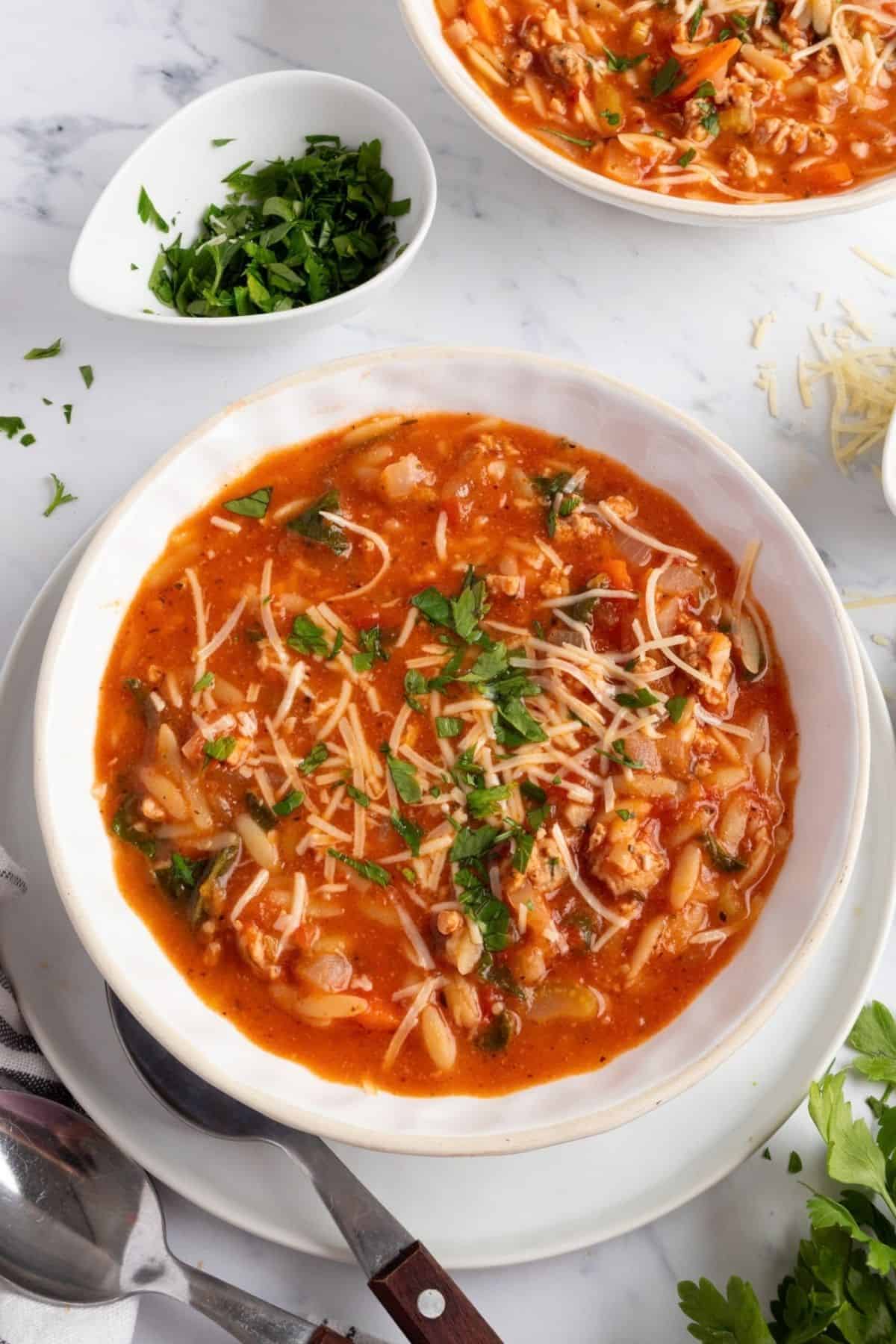 A bowl of creamy sausage orzo soup with spinach, topped with Parmesan and parsley