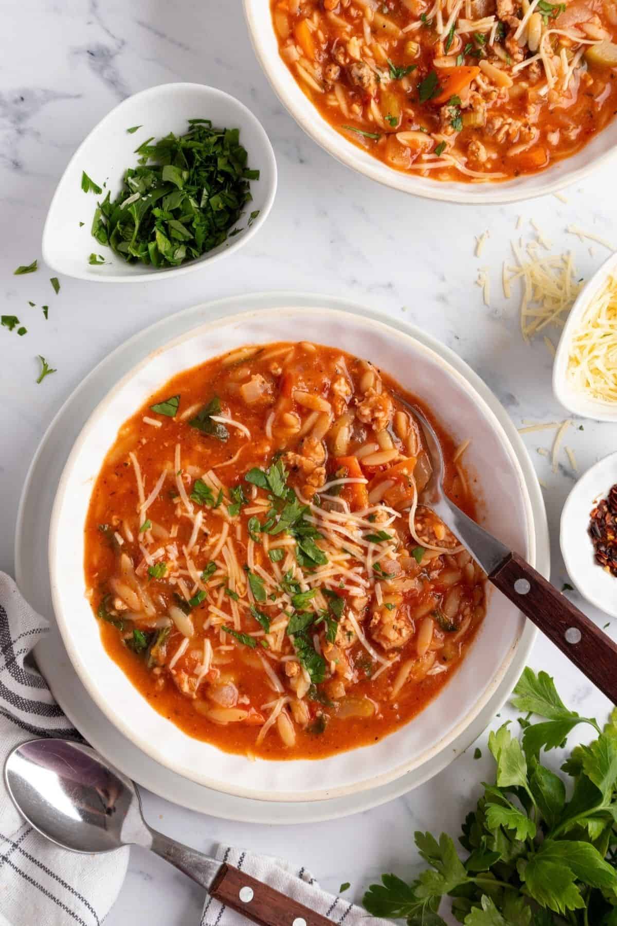 Two bowls of sausage orzo soup with a plate of Parmesan cheese to the side.