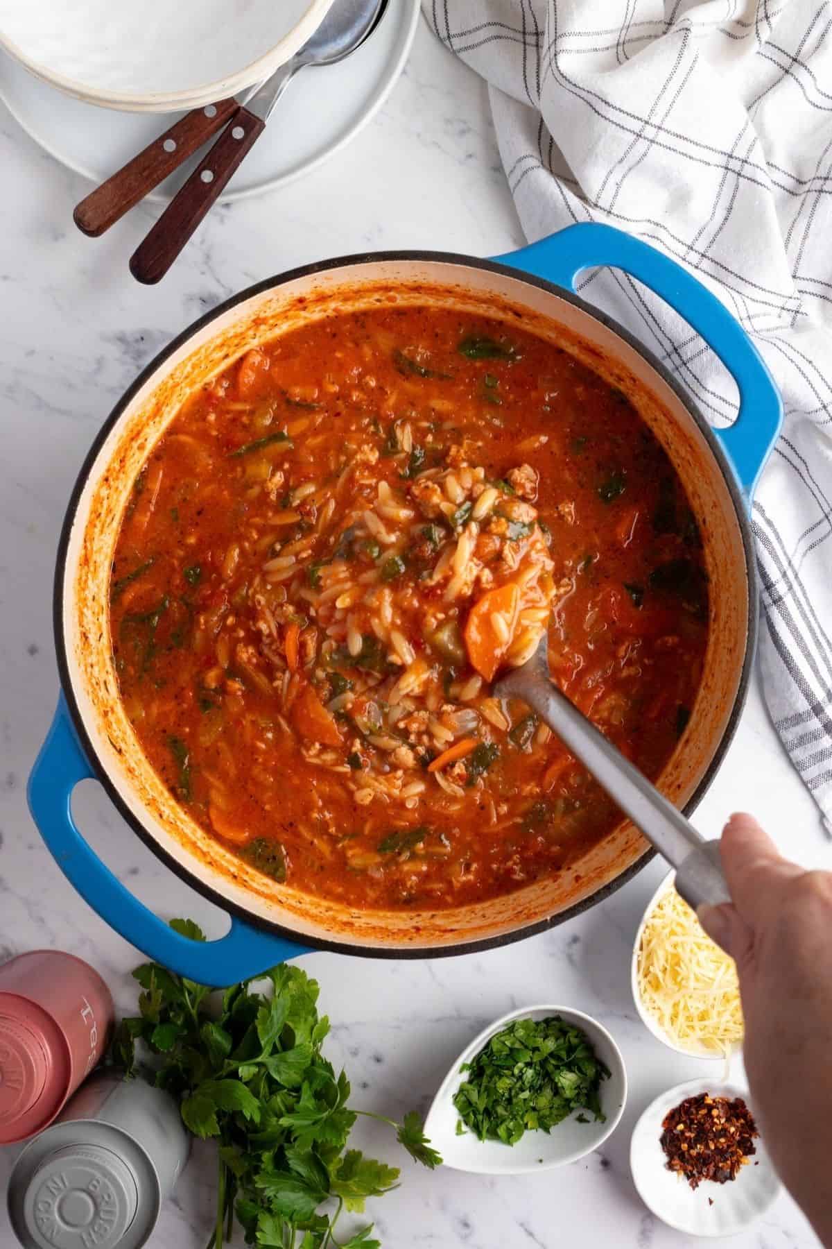 A ladle lifting creamy sausage orzo soup from the pot